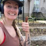 Woman with headphones and a brown tank top giving a thumbs up.