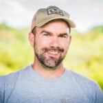 Man in grey shirt wearing a baseball cap.