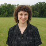 Woman wearing a black collared shirt in a green field.